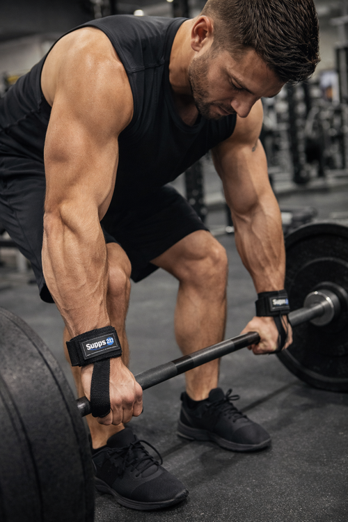 Man lifting weights with focus on his muscular arms and legs in a gym setting.